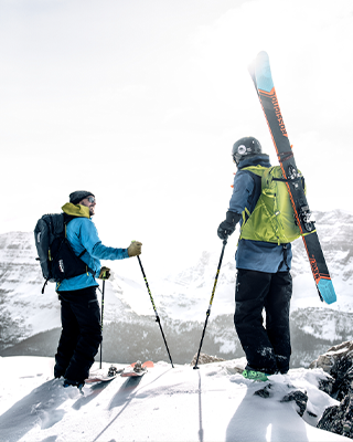 Twee mensen met ski's en ski rugzakken staan op een berg.